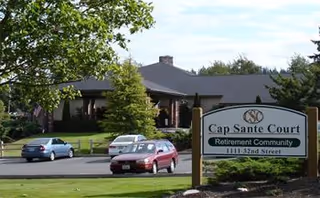 Front exterior view of Cap Sante Court Retirement Community with a sign and parked cars.