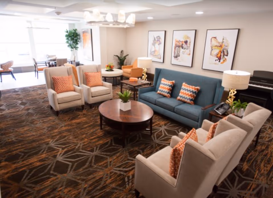 Bright furnished common living room with sofas, armchairs, coffee tables, patterned carpet and wall artwork.