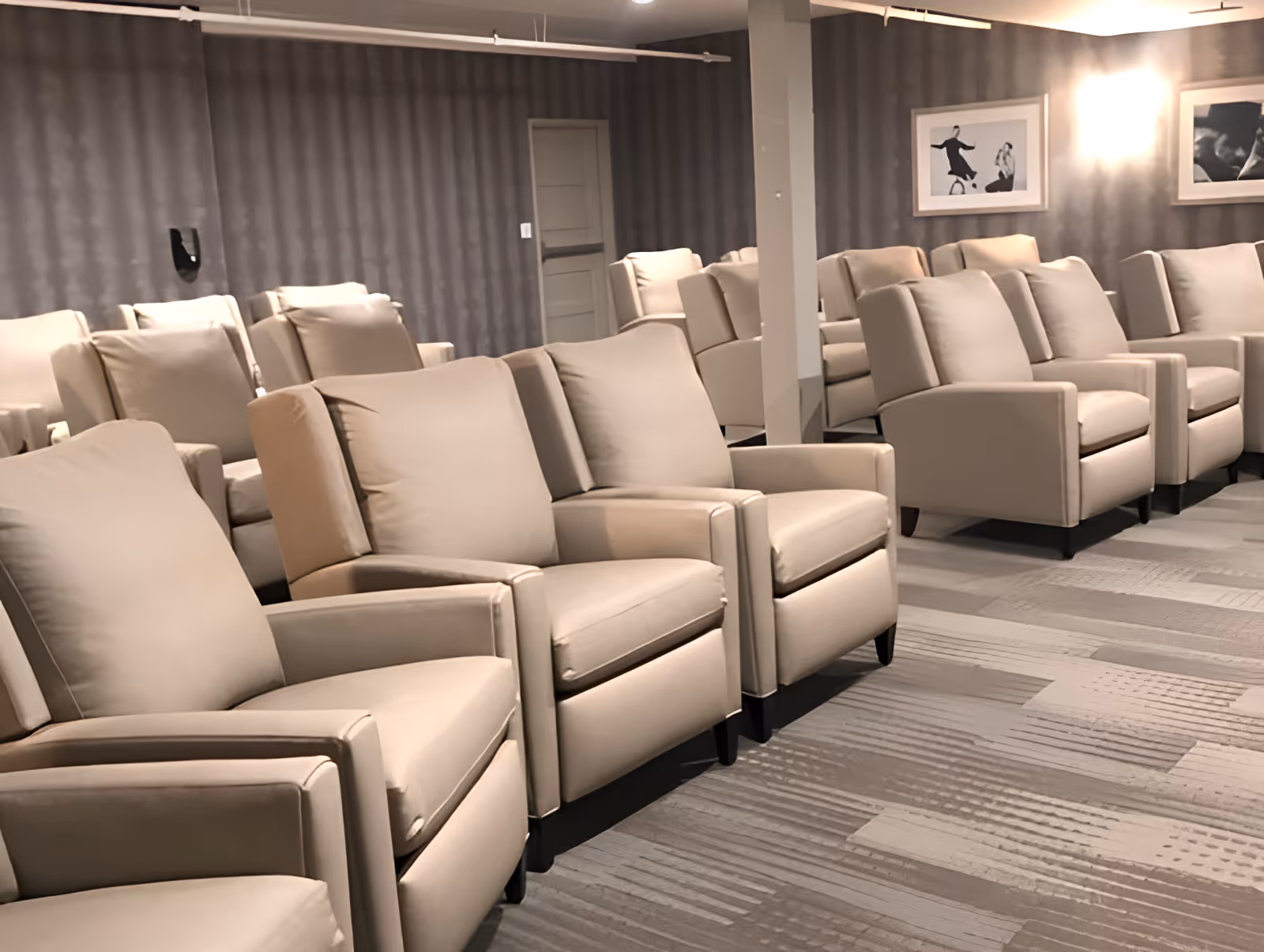 Rows of beige reclining chairs arranged in a carpeted interior room with framed pictures on the wall.