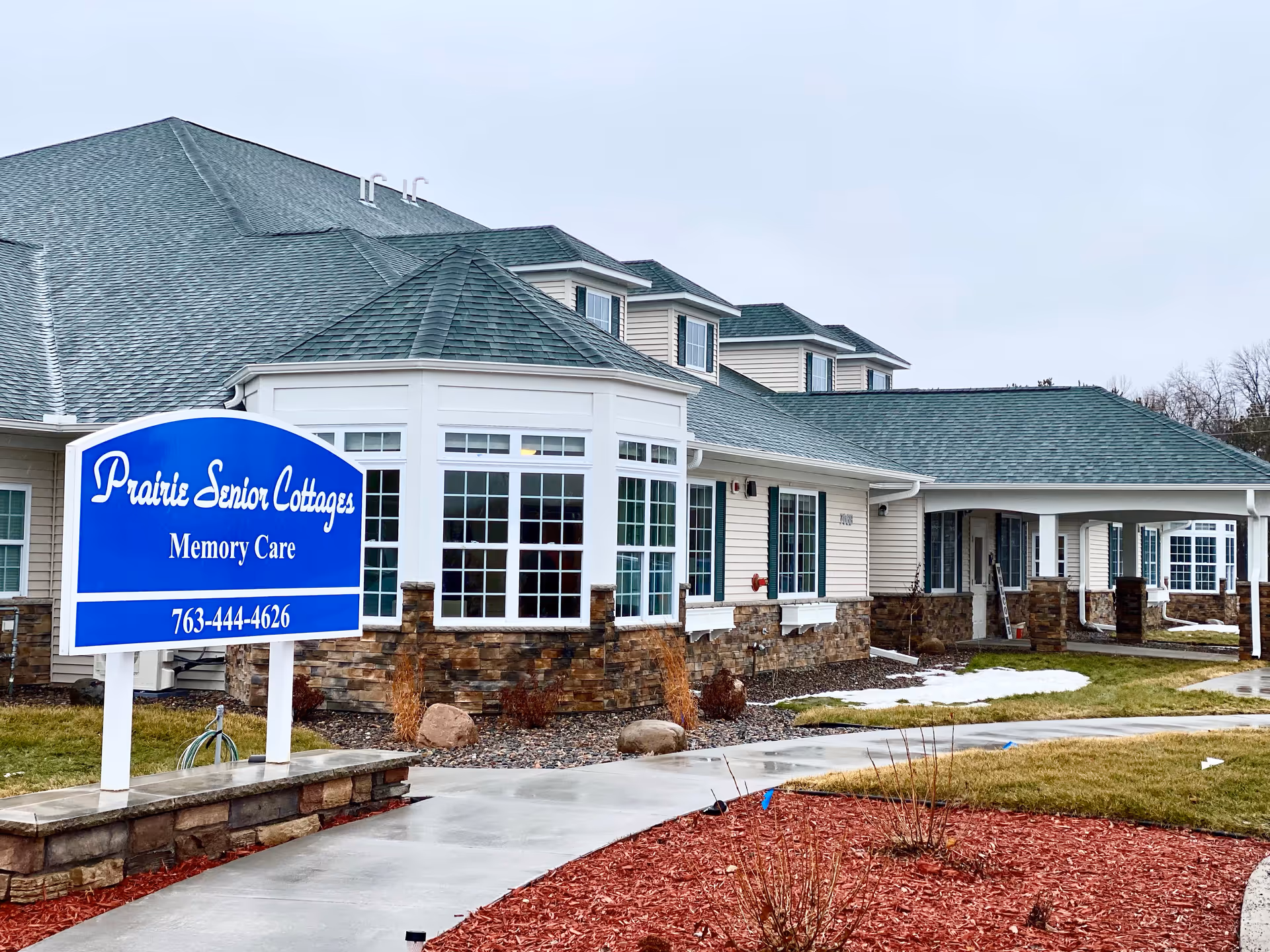 Front exterior of Prairie Senior Cottages memory care building with a blue sign and walkway.