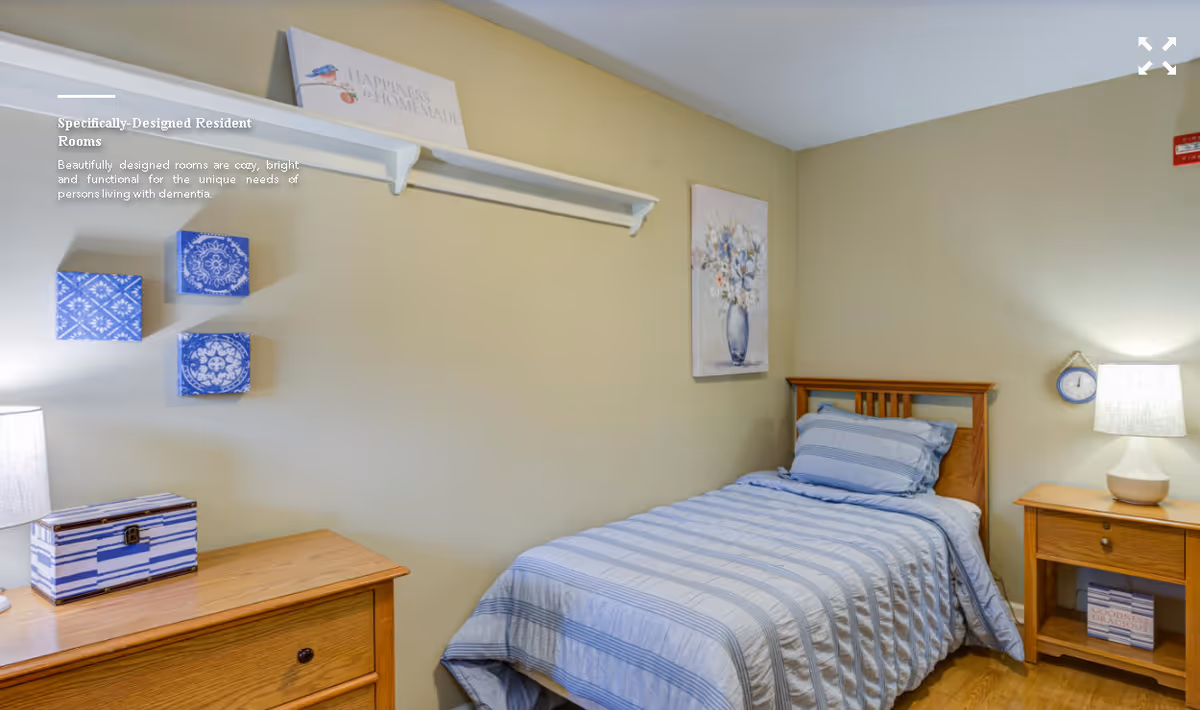 Small furnished single bedroom with a twin bed, wooden nightstand and dresser, blue-striped bedding and wall decor.
