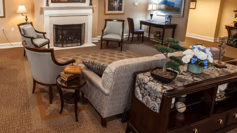 Comfortable furnished living room with a sofa, armchairs, fireplace, side tables, and decorative plants and flowers.