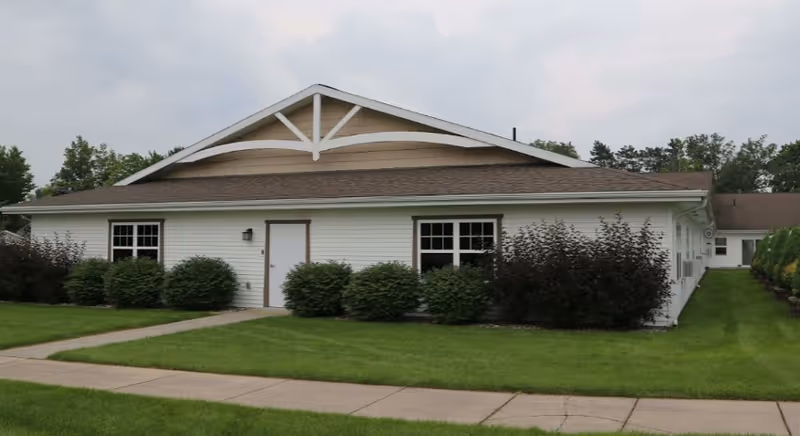 Single-story white building with shrubs and a sidewalk in front under a cloudy sky.