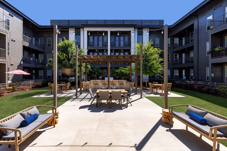 Courtyard patio with a pergola, seating and dining tables surrounded by a multi-story residential building.
