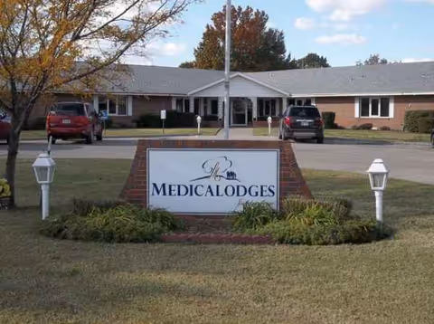 Front view of Medicalodges Independence facility with sign and parked cars
