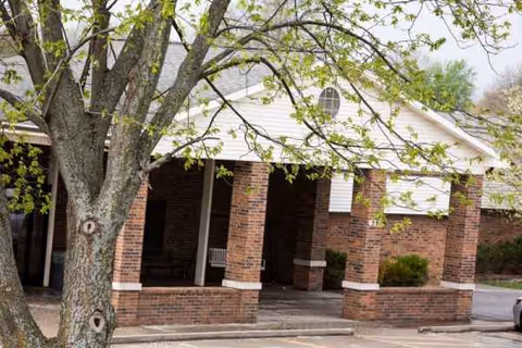 Brick building entrance with a covered walkway and a large tree in the foreground