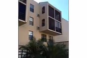Three-story beige assisted living building with enclosed balconies and palm plants in front.