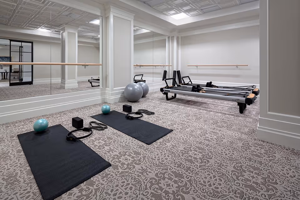 A bright mirrored fitness studio with Pilates reformers, yoga mats, exercise balls, and wall-mounted ballet barres.