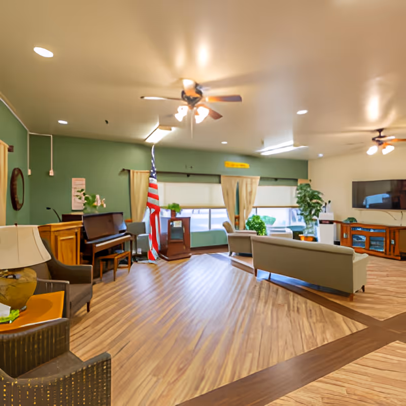 Spacious lounge area with sofas, armchairs, a piano, an American flag, TV, plants, and wood-pattern flooring.