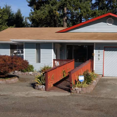 Front exterior of a blue, single-story AssureCare Adult Home with a red-railed ramp.