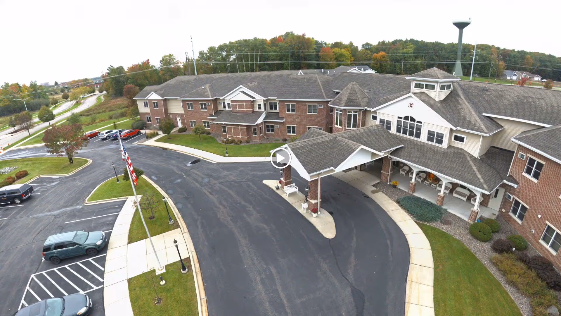 Aerial view of the Renaissance by Rennes - Weston brick senior living building with a covered front entrance, circular driveway, flagpoles and parked cars.
