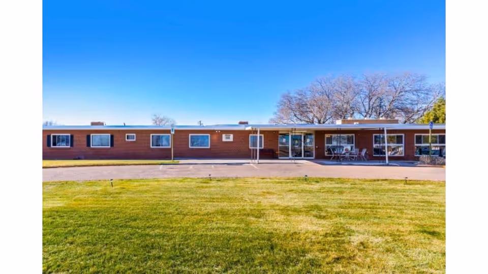 Single-story brick building with multiple windows and a glass entrance door, surrounded by a well-maintained green lawn under a clear blue sky.