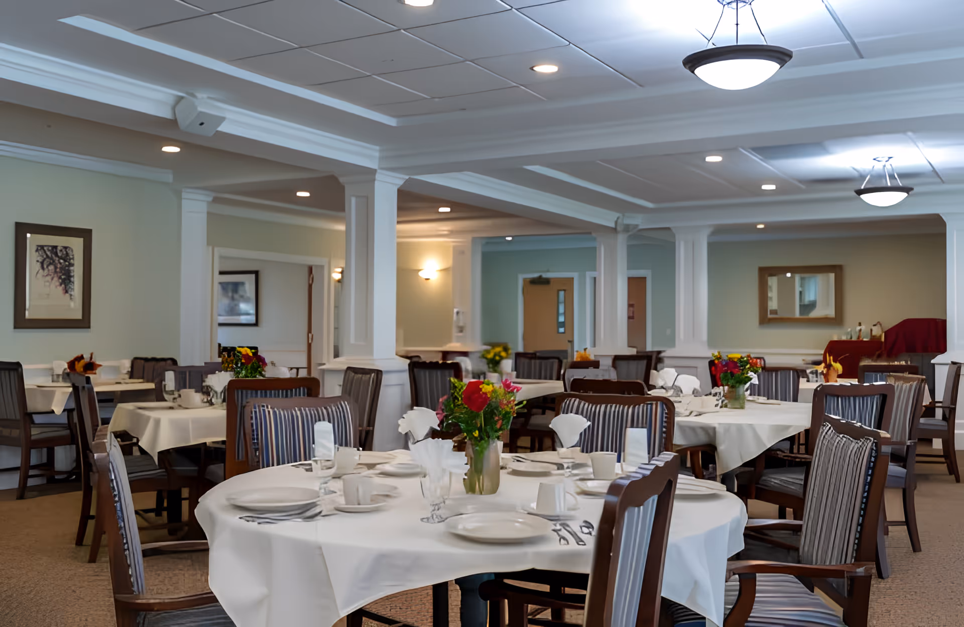 Formal dining room with round tables set with white tablecloths, place settings, and floral centerpieces.