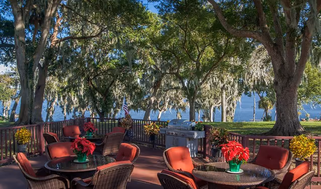 Outdoor patio with red cushioned chairs, tables, and trees overlooking a lake.