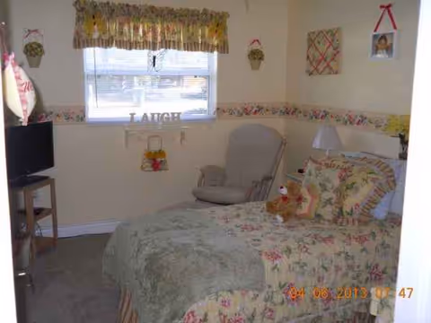 Cozy floral bedroom featuring a bed with quilt, window, rocking chair, and small TV.