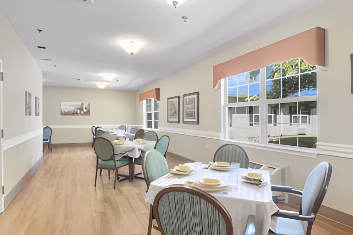Bright dining room with multiple set tables and chairs, large windows, and wood flooring.