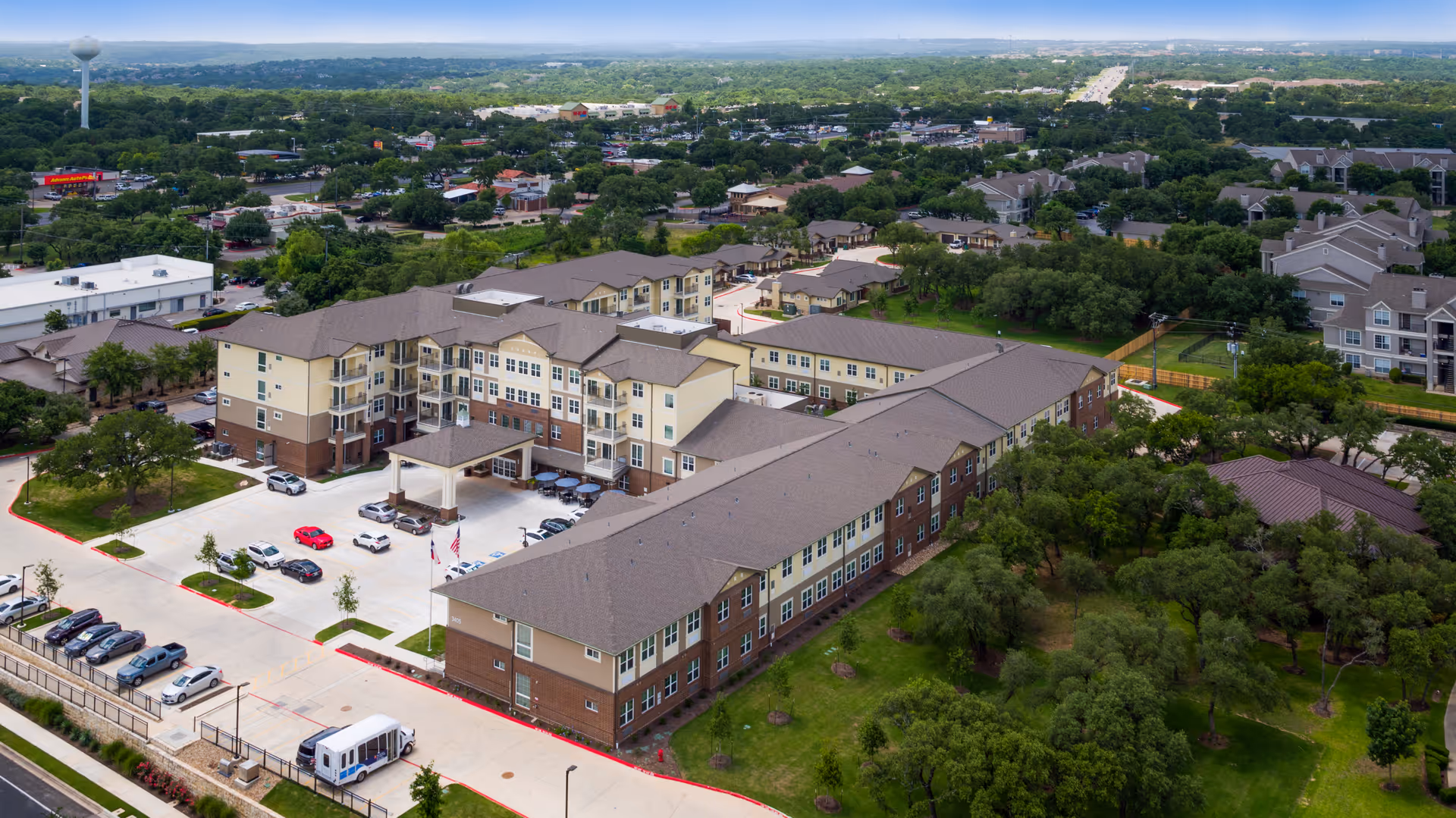 Aerial view of The Enclave at Cedar Park Senior Living showing multi-story buildings, a parking area, and surrounding trees and neighborhood.