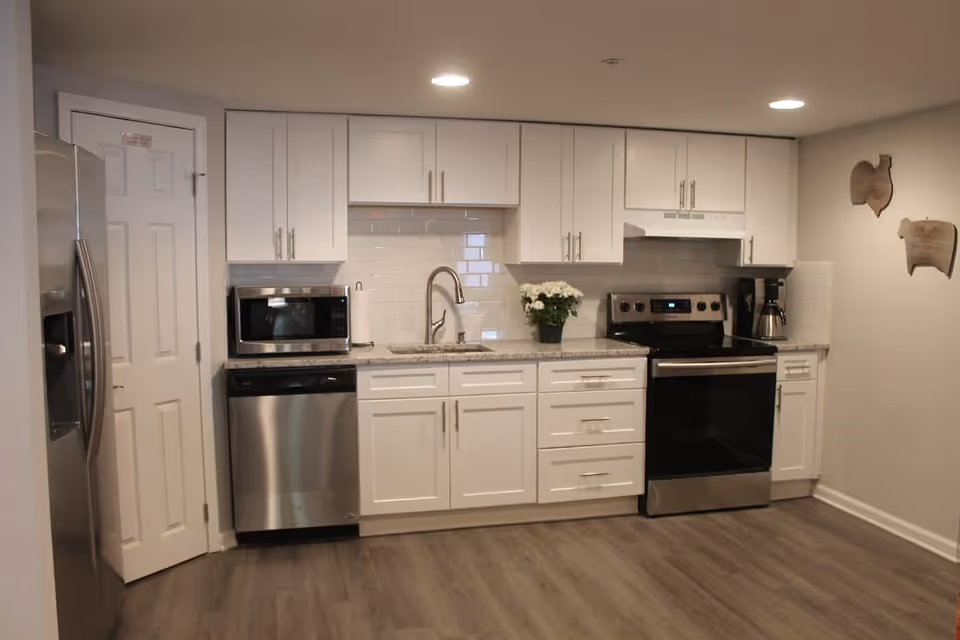 Clean modern kitchen with white cabinets, stainless steel appliances, subway tile backsplash, and wood-look flooring.