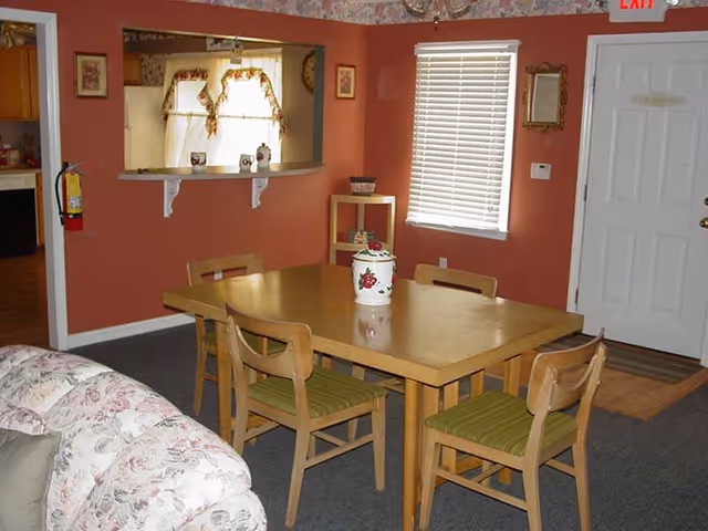 Dining room with wooden table and six chairs, red walls, and a window.