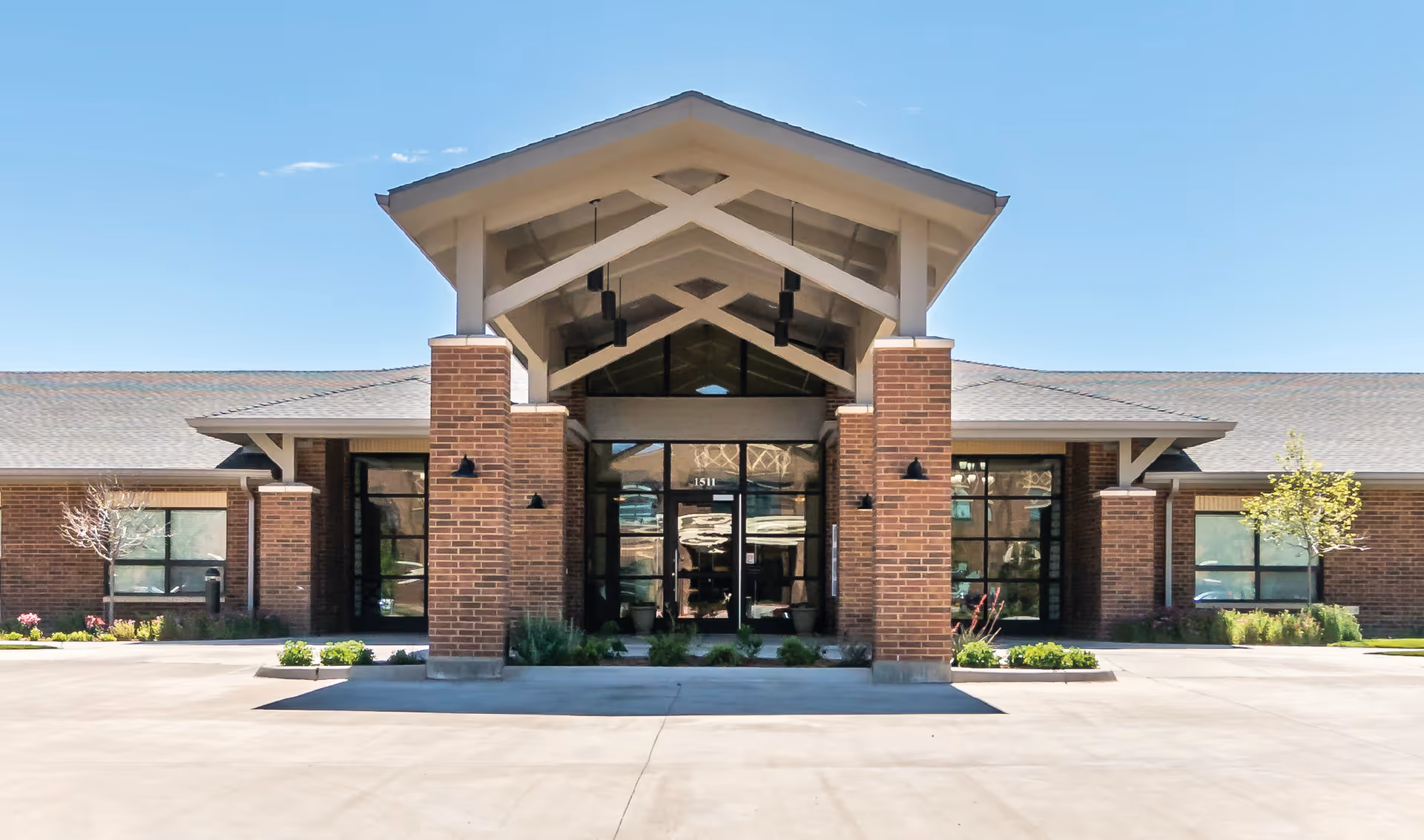 Front entrance of a single-story brick building with a large covered portico and glass double doors.