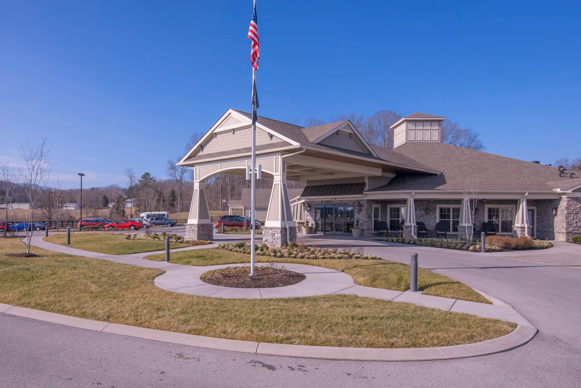 Exterior front entrance of Morning Pointe of Powell featuring a covered porte-cochère, flagpole, and landscaped driveway.