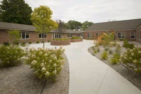 Exterior view of a senior living facility courtyard with brick buildings, paths, and greenery.