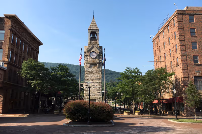 Stone clock tower in a brick-lined downtown plaza with trees and American flags.