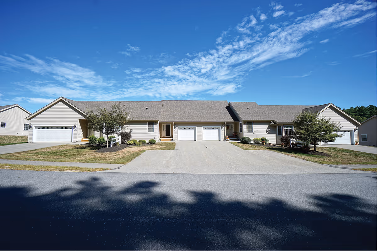 Front view of a single-story row of attached homes with garages and driveways under a blue sky.