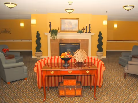 Lobby seating area with a striped sofa and wooden console table facing a fireplace flanked by decorative topiaries.