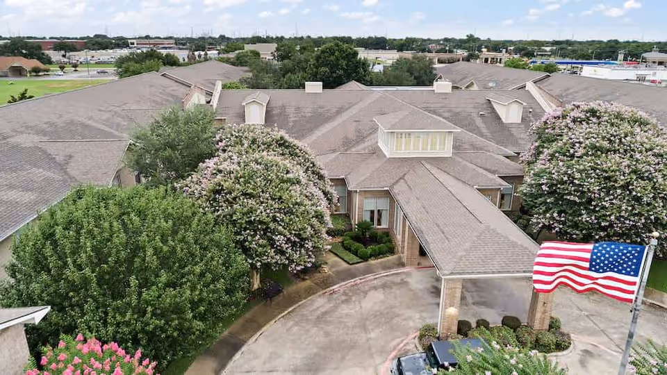 Aerial view of the Morada Deer Park entrance showing the building's roof, landscaped trees, circular driveway and an American flag.