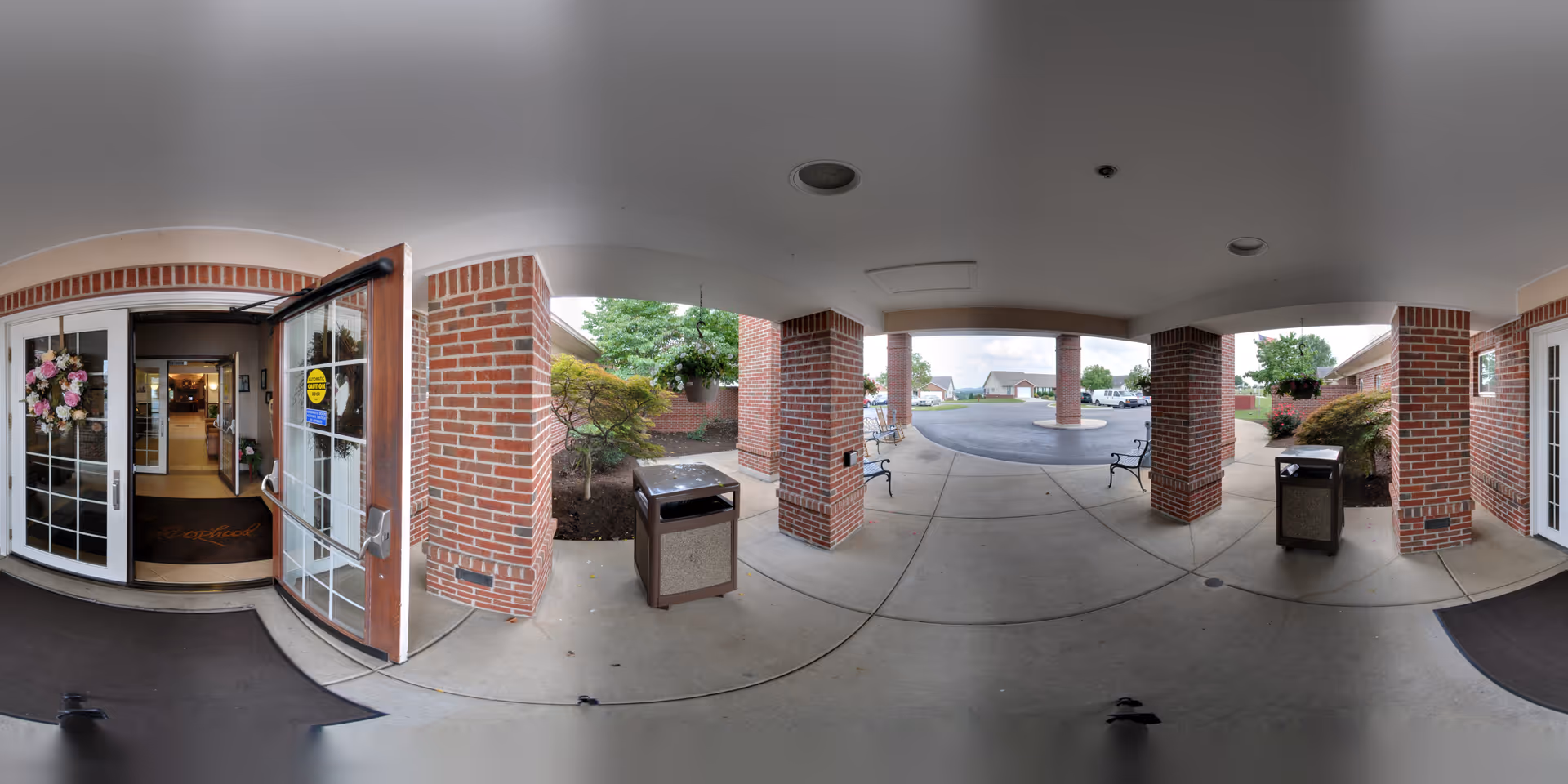 Covered brick porte-cochère and entrance with open glass double doors, benches, and trash receptacles.