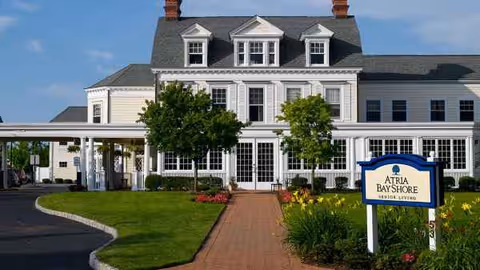 Atria Bay Shore exterior: a white, multi-story building with a brick walkway and manicured lawn.