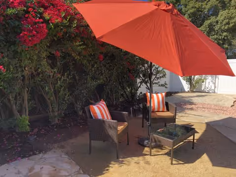 Outdoor seating area with wicker chairs, orange cushions, and a red umbrella.