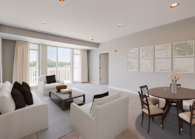 Bright open-plan living and dining area with white sofas, a coffee table, and a round dining table beside large windows.