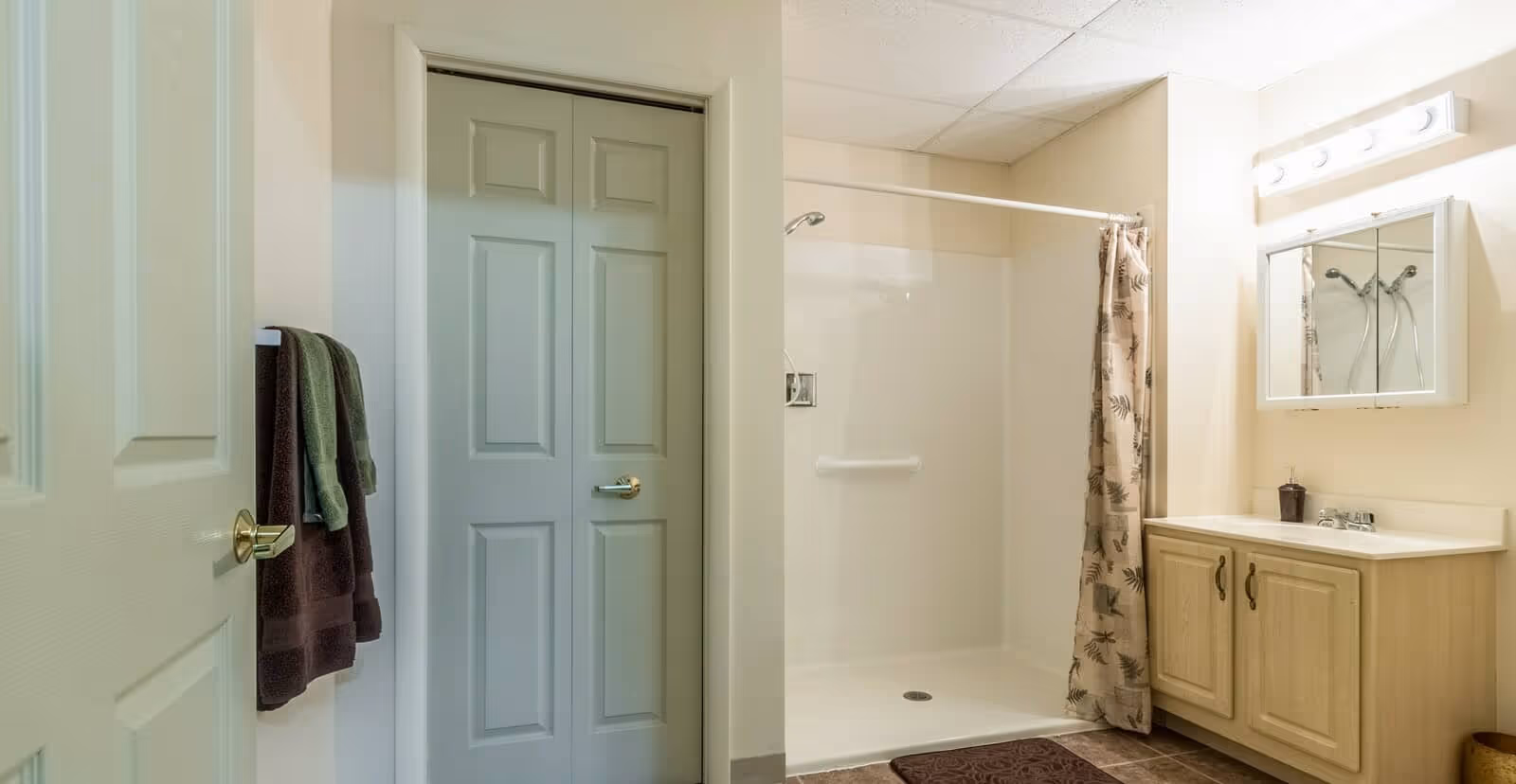 Clean bathroom with a walk-in shower, vanity with mirror and sink, and towels hanging on hooks.