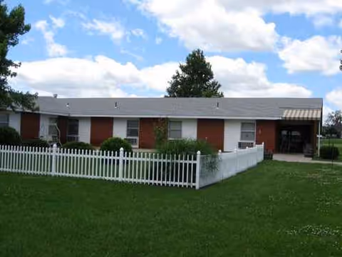 Single-story brick senior living facility with a white picket fence and green lawn.