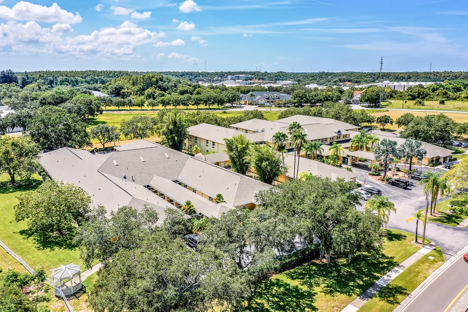 Aerial view of a senior living facility named Sun City Senior Living surrounded by trees, green lawns, and parking areas under a partly cloudy sky.