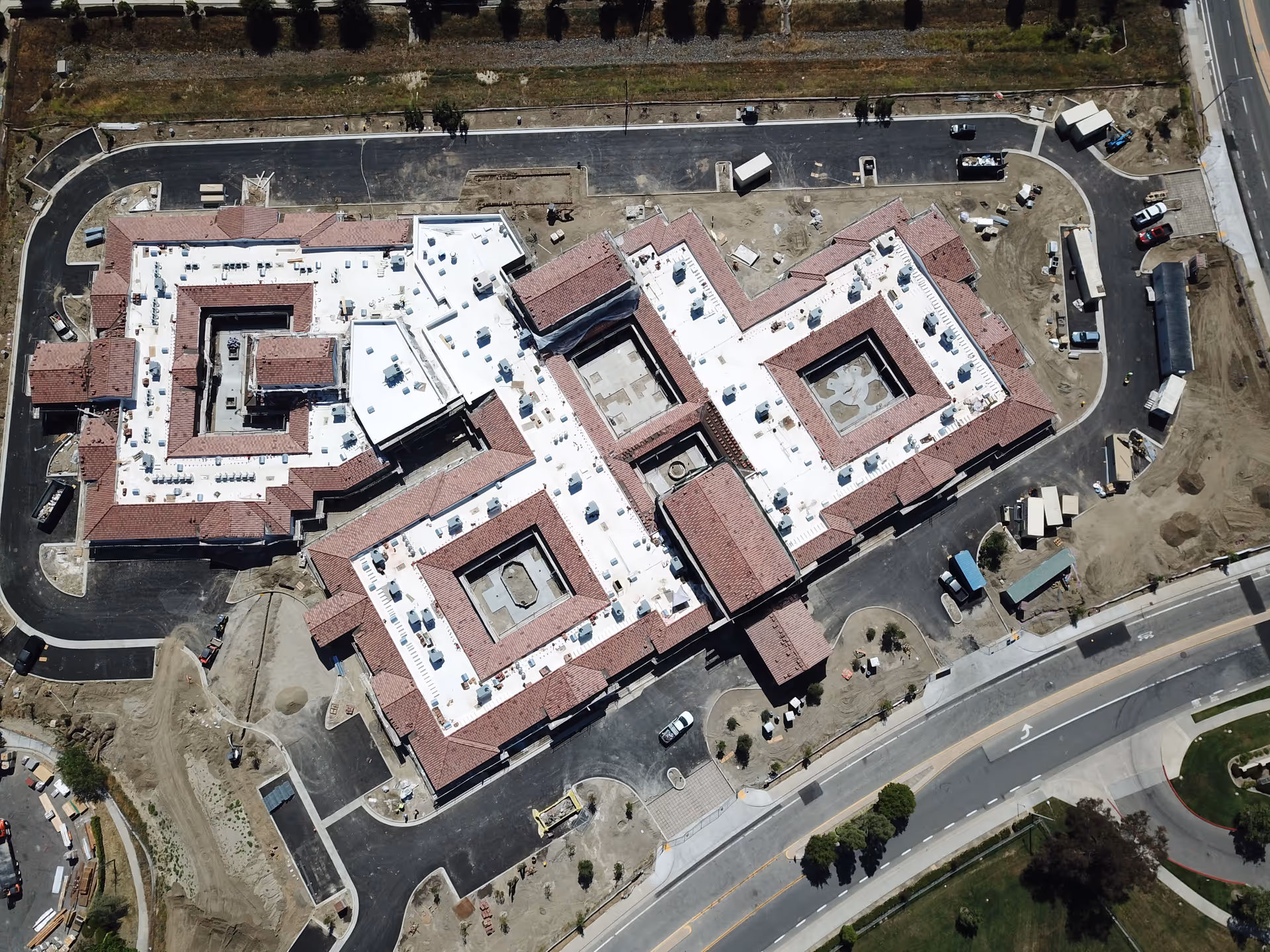 Aerial view of a large multi-wing senior living building under construction with central courtyards, surrounding roads, and construction equipment.
