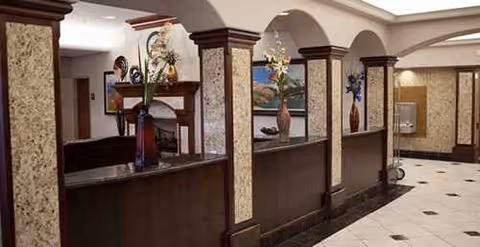 Lobby reception area with dark wood desk, arches, columns, and decorative plants.