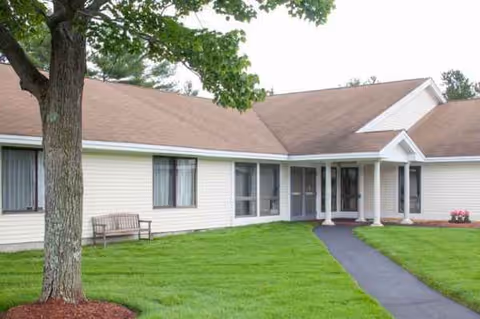 Single-story senior living facility exterior with beige siding, green lawn, and a walkway.