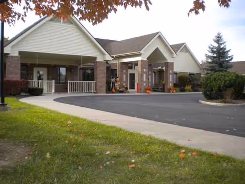 Senior living facility entrance with a covered drive, brick pillars, and potted plants.