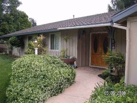 Front exterior of a single-story care home with wooden doors and manicured shrubs