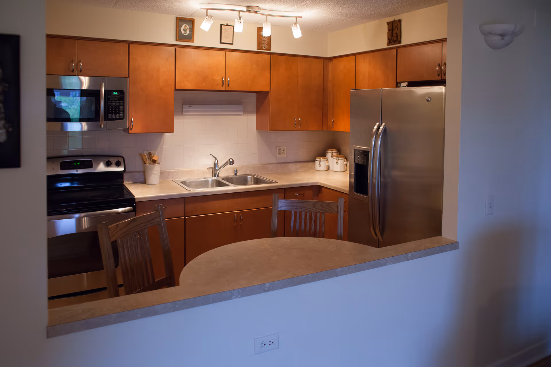 Open kitchen with wood cabinets, stainless steel appliances, a double sink and a curved breakfast bar with chairs.