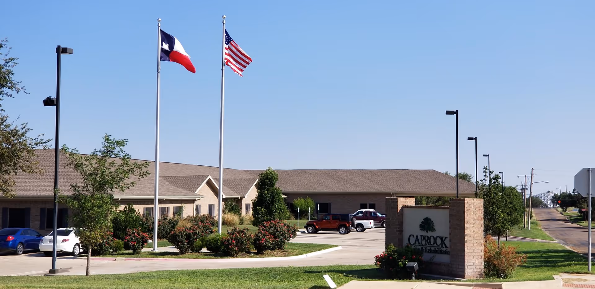 Front exterior of Caprock Nursing and Rehabilitation Center with American and Texas flags and a brick entrance sign.