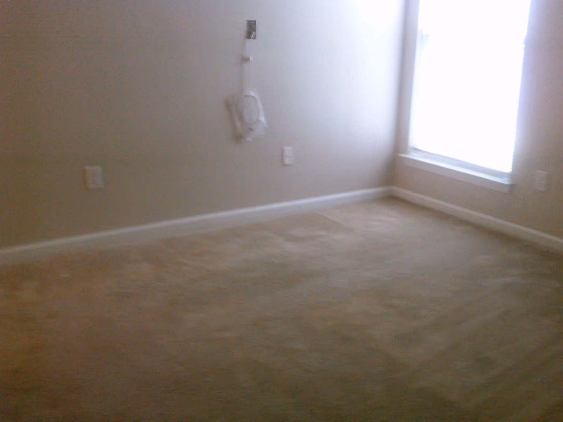 Empty carpeted room with beige walls and a bright window.