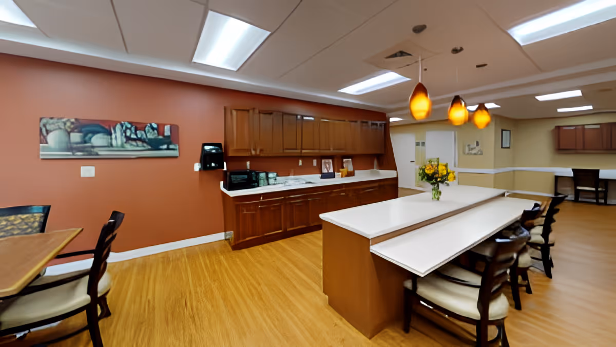 A communal dining area with a long white island and bar stools, wooden cabinets and pendant lights.