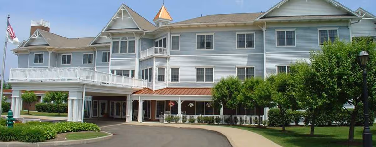 Front exterior of a multi-story white senior living building with a covered entrance, balcony, and landscaped driveway.