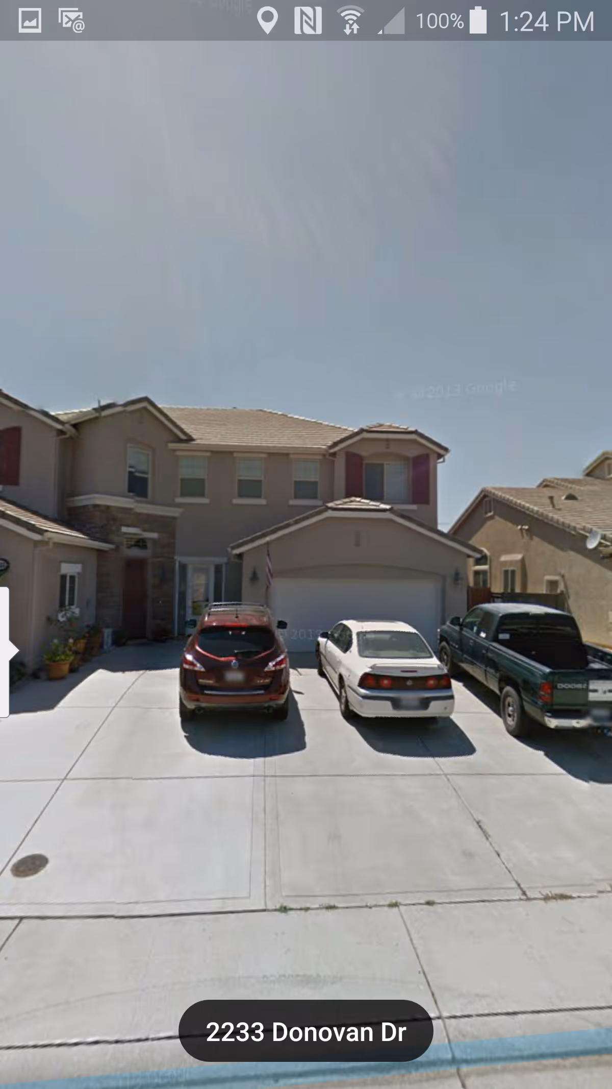 Front exterior view of a two-story residential building with a three-car driveway. Three vehicles are parked in the driveway in front of a garage. The house has beige walls, a tiled roof, and red shutters on some windows.