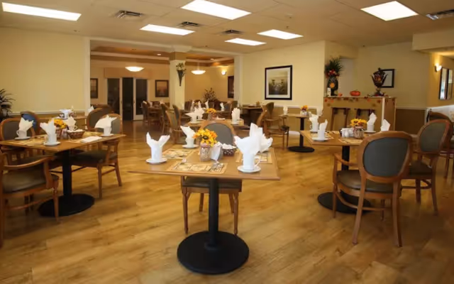 Dining room with neatly set tables and chairs, folded napkins and floral centerpieces.