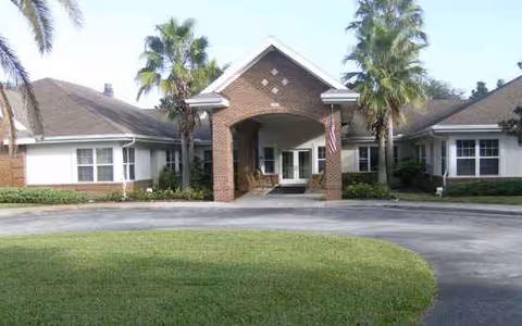 Exterior view of a senior living facility entrance with a circular driveway and palm trees.